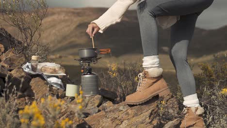 side view slow motion footage of a woman cooking noodles in a tiny pot on top of a mountain