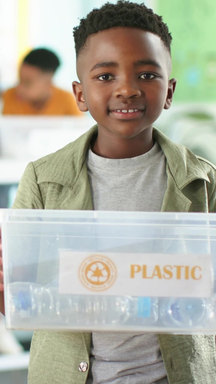 Video verticale: Ragazzo in verde che tiene un contenitore di PLASTICA con bottiglie in classe, al segnale per il riciclaggio.