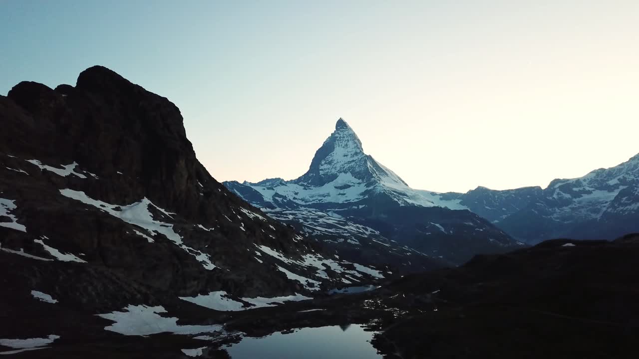 Drone shot of Matterhorn peak reflecting in the calm waters of Riffelsee lake at dawn, creating serene landscape in Zermatt, Wallis, Switzerland