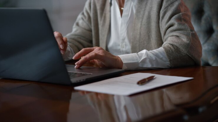 Mani di donna anziana che lavorano al laptop a casa.