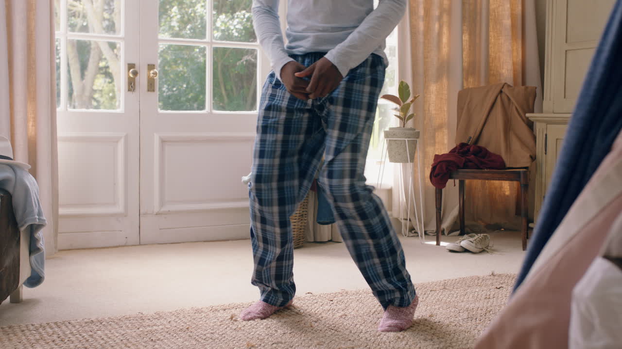 uomo afroamericano divertente che balla in camera da letto che si diverte a festeggiare sentendosi positivo che gode di uno stile di vita di successo che balla sciocchi a casa la mattina del fine settimana indossando il pigiama