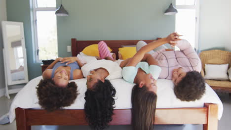 felices amigas diversas acostadas en la cama y sonriendo en el dormitorio