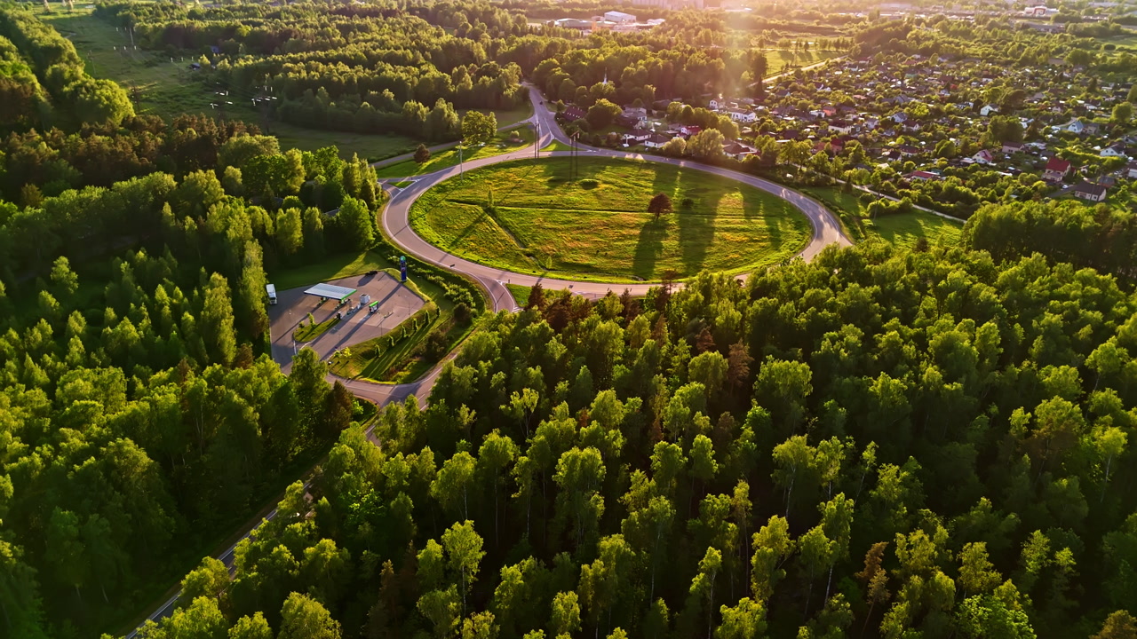 Aerial view of large roundabout intersection surrounded by forest and residential neighborhood in warm golden hour light