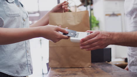 primer plano de una mujer en una tienda haciendo un pago sin contacto en el mostrador de ventas sosteniendo una tarjeta de crédito para el lector