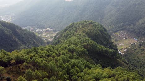 Un-Vuelo-Aéreo-Sobre-Las-Estribaciones-Boscosas-De-Las-Montañas-Del-Himalaya-En-Nepal-Para-Revelar-Un-Pequeño-Pueblo-En-El-Valle