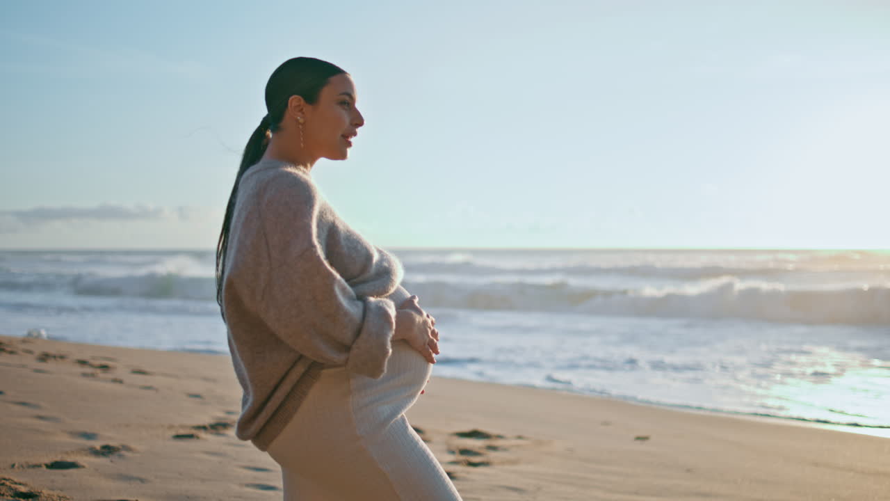 женщина, ожидающая ребенка, смотрит на вечерний морской пейзаж на пляже. беременная девушка