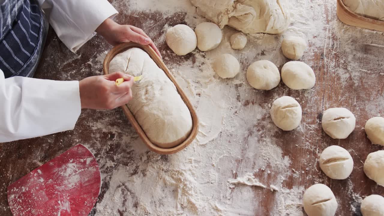Padeira asiática trabalhando na cozinha da padaria, cortando a massa para pão em câmera lenta.