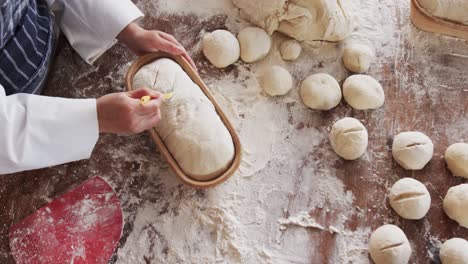 asian female baker working in bakery kitchen, cutting dough for bread in slow motion