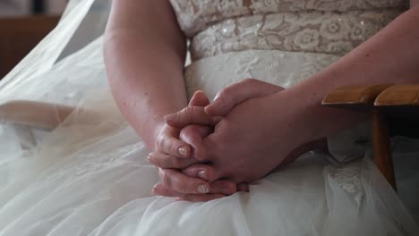 bride sitting in a white dress, hands clasped together, close-up shot