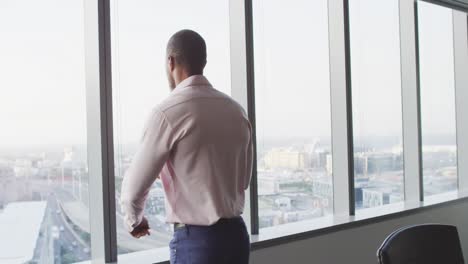 Un-Hombre-De-Negocios-Profesional-Reflexivo-Mirando-Por-Una-Ventana-Desde-Su-Oficina-Moderna-En-Cámara-Lenta