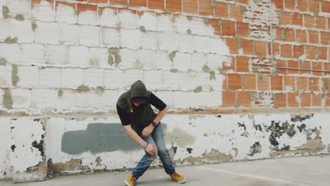 man hip hop dancing outside in city in front of brick wall