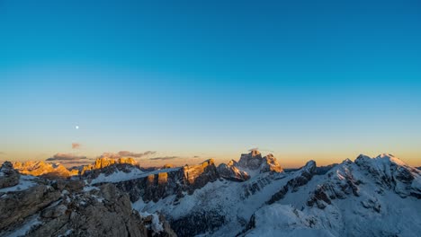 Tiro-De-Lapso-De-Tiempo-De-La-Hermosa-Puesta-De-Sol-En-El-Horizonte-Y-La-Luna-Llena-En-Ascenso-En-El-Cielo-Sobre-Las-Cumbres-De-Las-Montañas-Nevadas