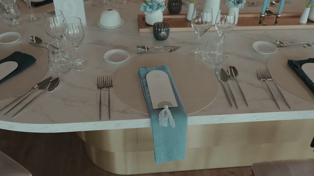 Elegante montaje de mesa para boda con servilleta azul, cubertería plateada, copas de vino y menú.