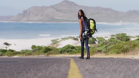 Mujer-Afroamericana-Con-Mochila-Tratando-De-Enganchar-Un-Ascensor-Mientras-Camina-Por-La-Carretera