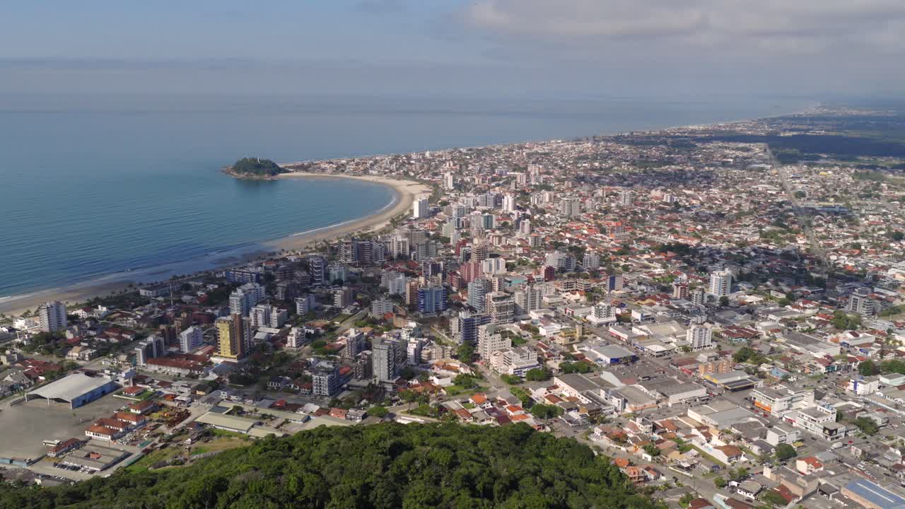 Amazing aerial fly over the Guaratuba city with crowded city blocks and sandy beach by the ocean, Paraná, Brazil