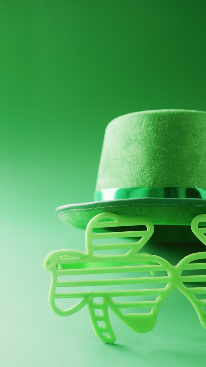 Vertical video of of st patrick's green hat and shamrock glasses with copy space on green background