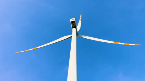 a towering wind turbine with three long blades against a clear blue sky, representing renewable energy and modern technology