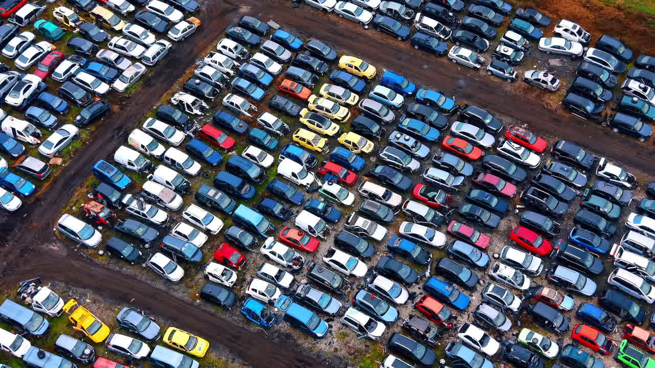 Højt vinkelperspektiv af bilkirkegård og jordveje. Droneperspektiv af forskellige beskadigede køretøjer parkeret i rækker med synlige jordstier og efterårsgræs i nærheden.