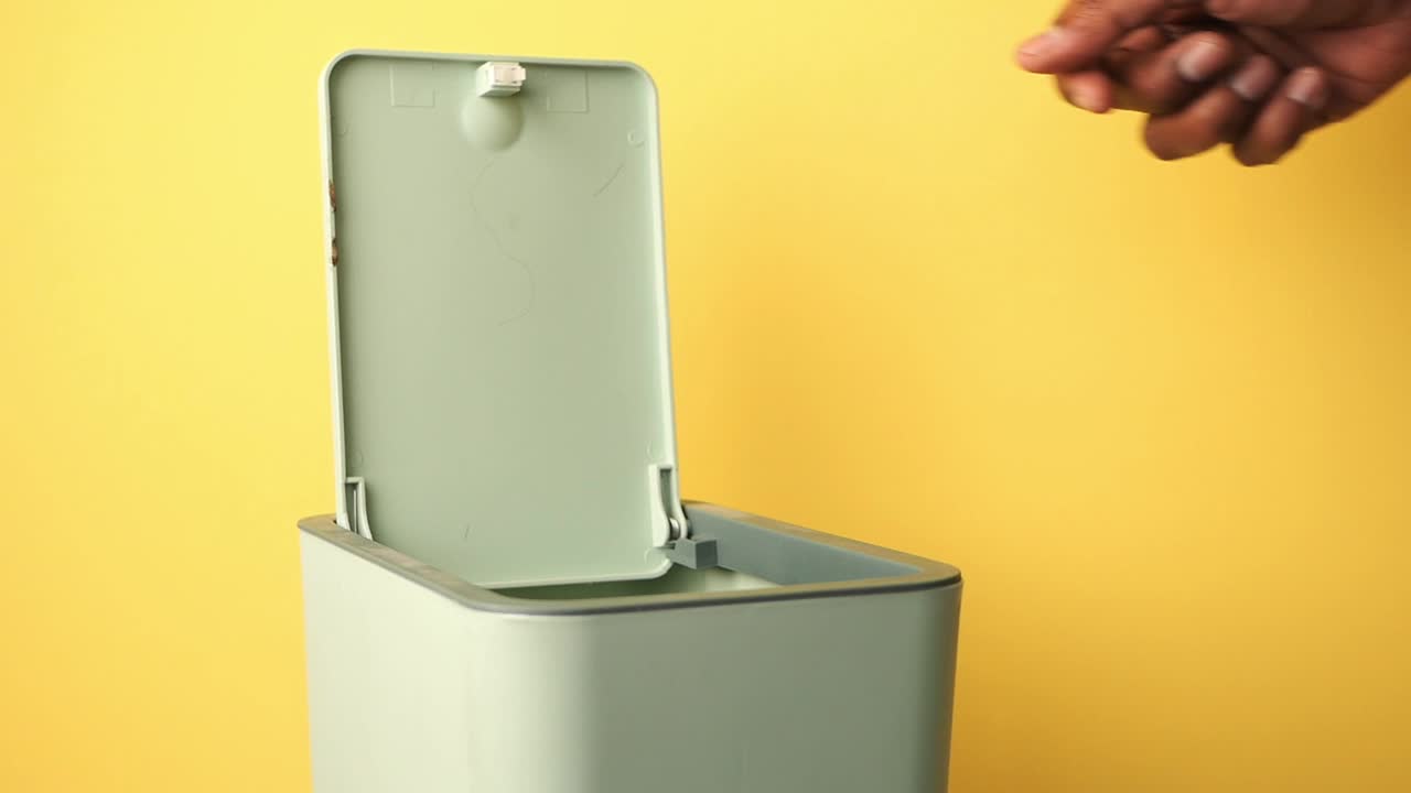 A hand opening a trash can
