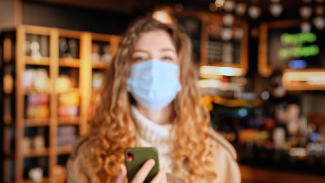 Donna con mascherina medica che mostra uno smartphone con il certificato di vaccinazione internazionale COVID-19 in un bar. Dose di richiamo, interni del bar