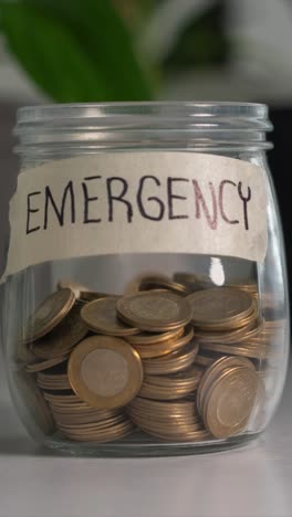 time-lapse saving money for emergency concept. coins into glass jar on desk. vertical