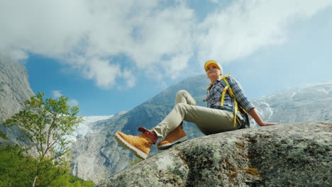 A-Woman-Is-Sitting-On-A-Big-Stone-Surrounded-By-The-Picturesque-Nature-Of-Norway-Mountains-And-Glaci