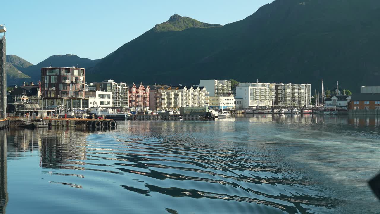 A ferry departs Svolvær on a calm early morning, with peaceful waters and the city’s buildings slowly fading into the distance