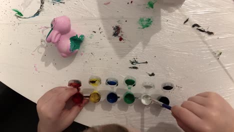 top view. the child is soaking the brush in the paint container. creative play with paint