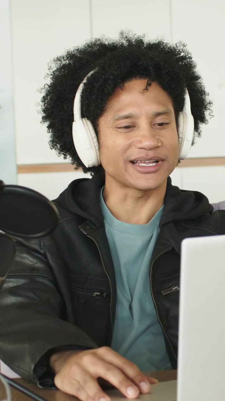 Vertical video: Checking laptop man at desk in coat, headset scrolling, speaking to mic for podcast