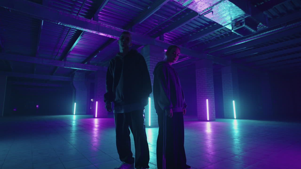 Duetto di giovani ballerini (uomo e donna) che ballano hip hop street dance in studio su sfondo nero. Giovani ballerini che si esercitano in una routine di ballo di notte con luci al neon. Ballerini professionisti che ballano hip hop