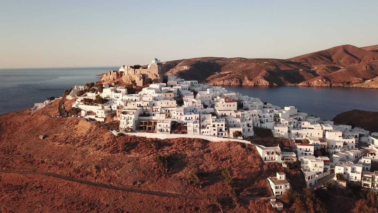 Greece,Astypalea Castle and town, drone footage from a distance on a sunny day early in the morning, no people.Traditional Greek houses are shinning. Behind the castle lies the deep blue Aegean Sea.