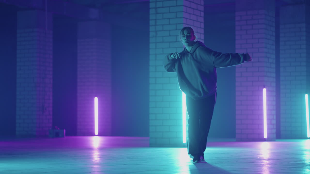 A steel woman dances hip-hop freestyle in a modern style in a hall with neon light in purple blue colors. Female Professional Hip Hop Dancer