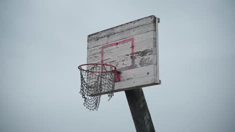 old basketball hoop with torn net hanging in wind and peeled off paint