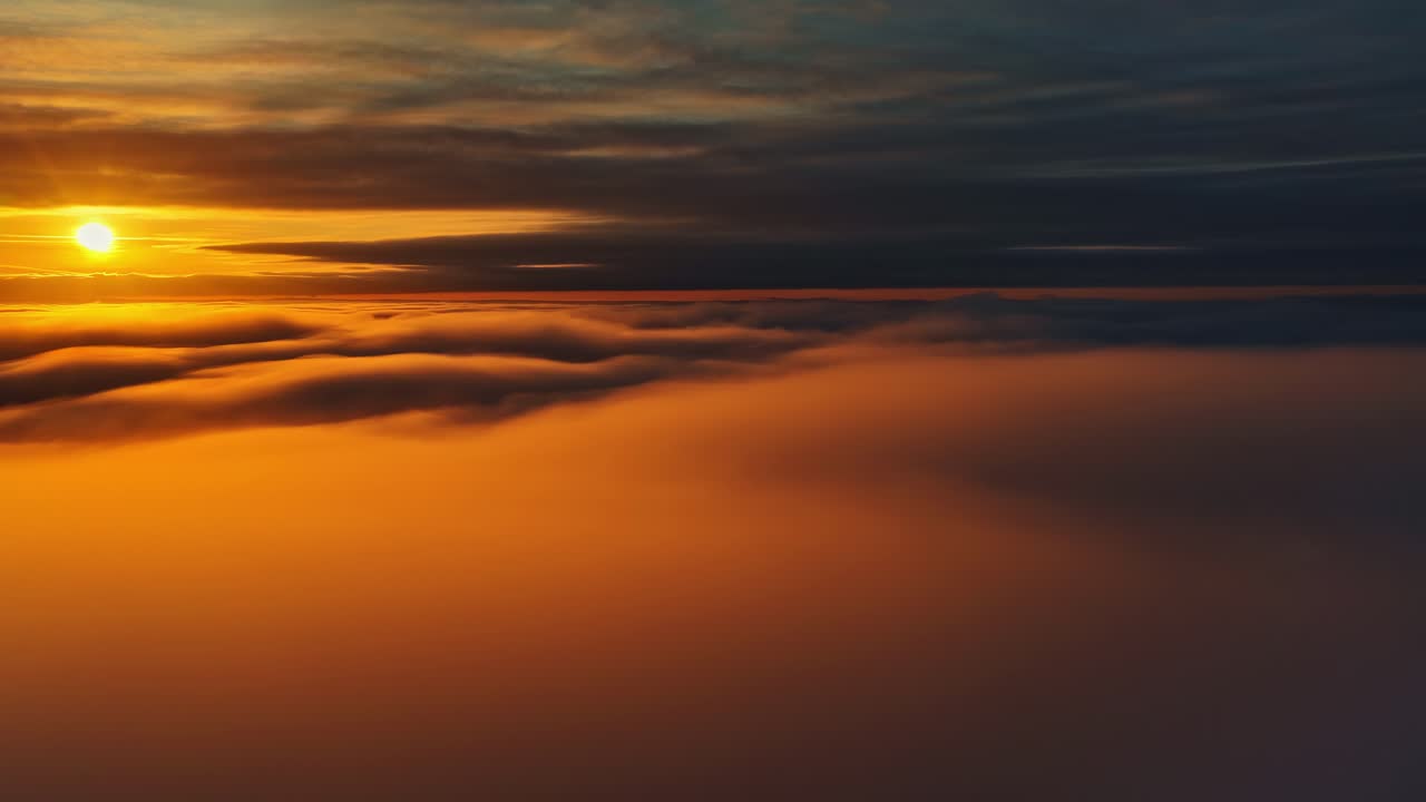 Goldenes Sonnenuntergangslicht ergießt sich über eine sanfte Wolkendecke, während die Kamera nach links schwenkt und sanfte atmosphärische Schichten in warmen Abendtönen enthüllt.