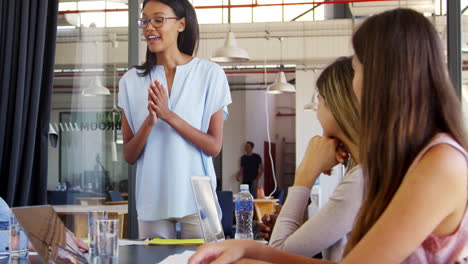 Young-woman-standing-claps-with-seated-colleagues-at-meeting