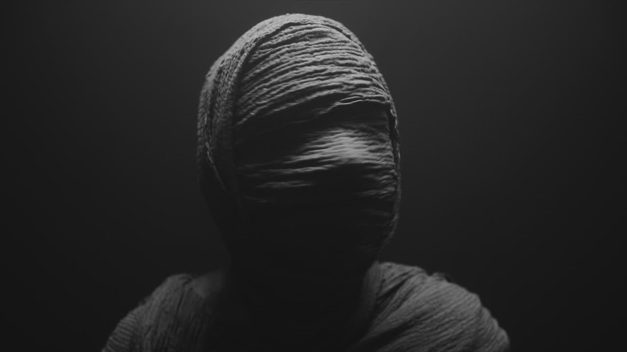 A mummy of a woman on a dark backdrop rises  and then turns her head