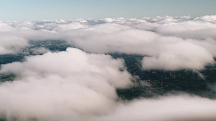 Thick white clouds floating above green countryside and forest landscape with small rural roads and settlements visible below.