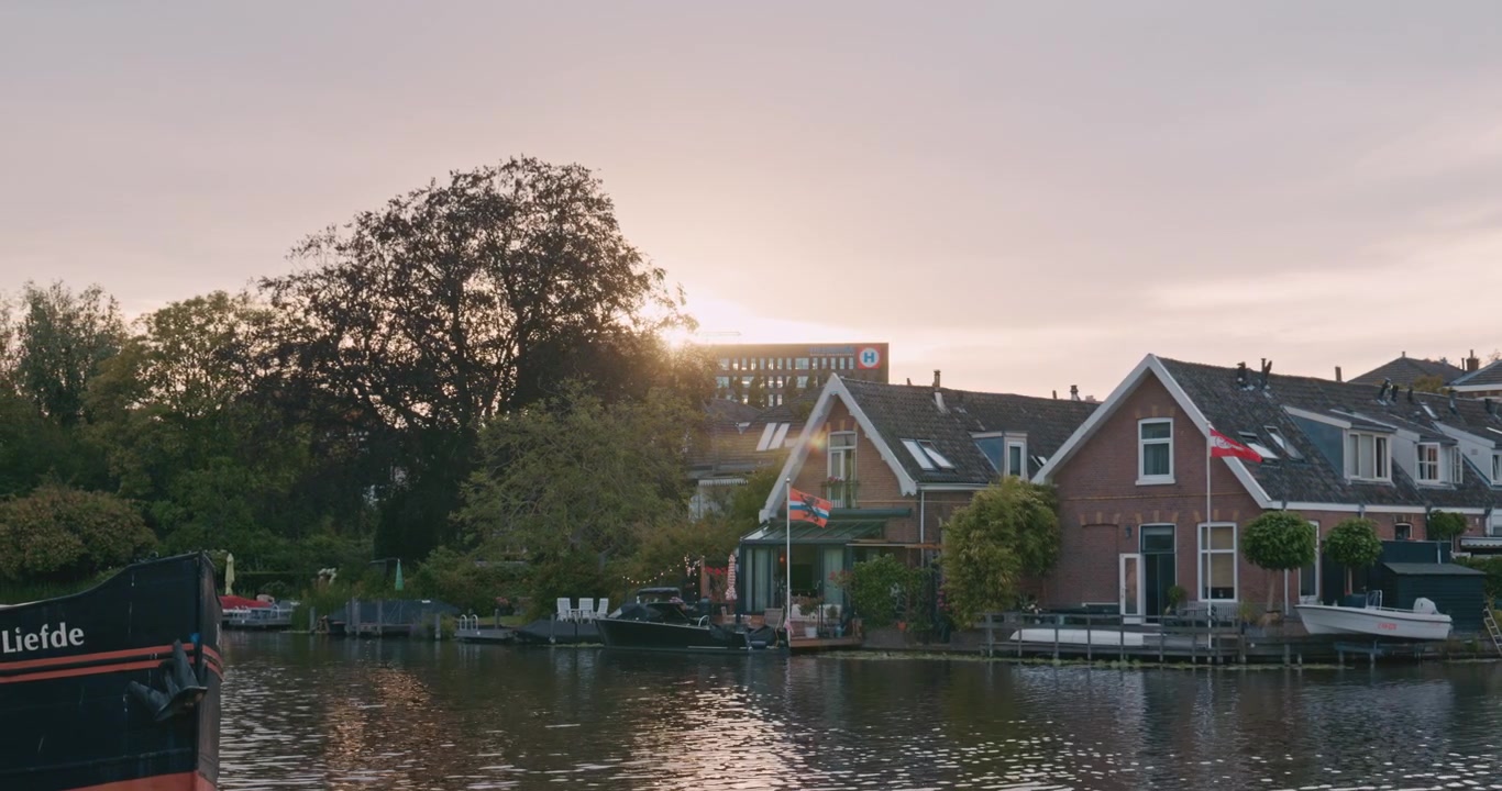 Tranquille case lungo il fiume a Leida, Paesi Bassi, Europa al tramonto con luce calda che filtra tra gli alberi e barche ormeggiate lungo la riva