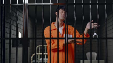 asian male prisoner standing in prison, smiling, showing the handcuffs and pointing to them