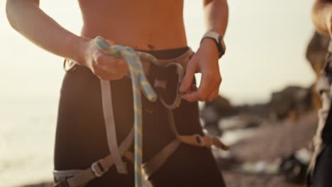 Close-up-shot-of-a-girl-in-black-pants-putting-a-special-belay-on-her-belt-and-tying-a-knot-in-a-special-rope-to-safely-climb-up-a-rock-while-rock-climbing-on-the-seashore