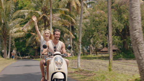 fun couple riding scooter on tropical island happy woman celebrating with arms raised enjoying vacation road trip with boyfriend on motorcycle ride