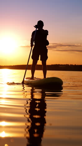 silhouette of a man confidently standing on the sup board. sportsman rows with an oar approaching camera. low angle view. vertical video.