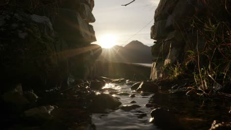 Die-Sonne-Geht-Hinter-Einem-Schottischen-Berg-Unter,-Um-Im-Hintergrund-Einen-Sunburst-Zu-Erzeugen,-Während-Ein-Kleiner-Fluss-Sanft-Unter-Einem-Bogen-In-Einer-Steinmauer-Fließt