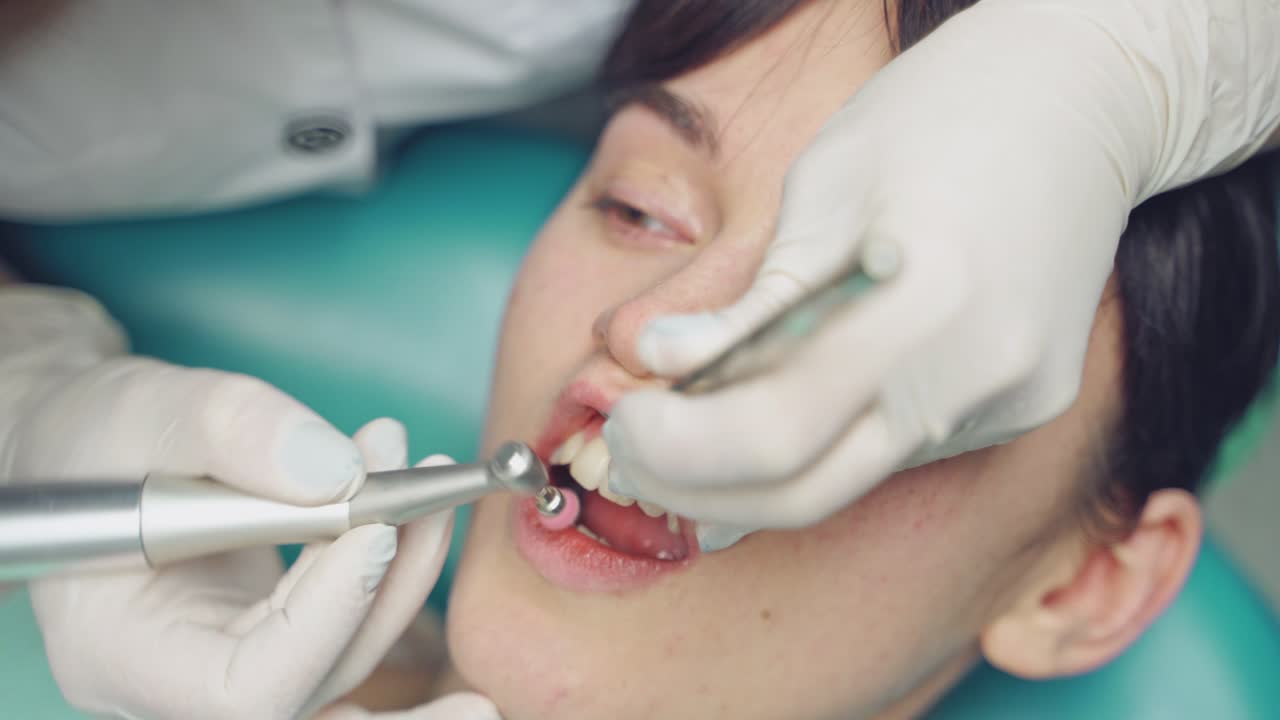 Professional dentist working with patient at dental office. Air flow method of cleaning teeth with sandblasting machine. Close-up