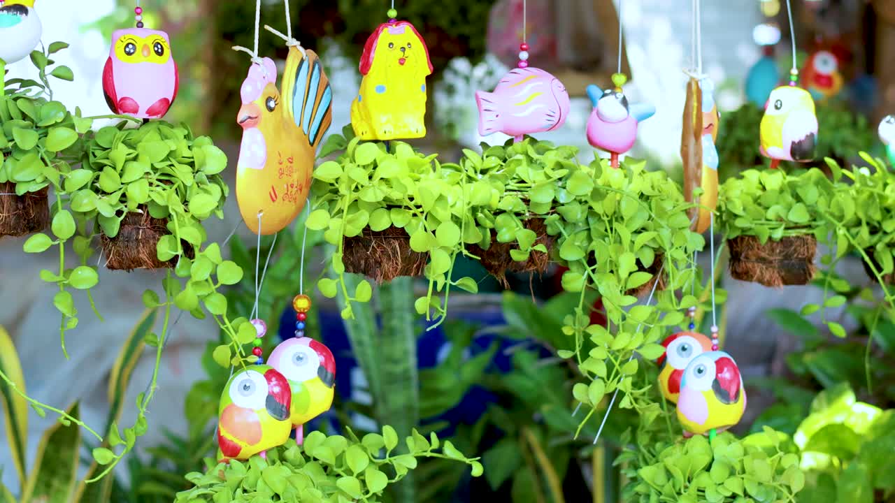Vibrant hanging ornaments sway gently among lush greenery, creating a lively and whimsical garden scene with bright colors and playful designs