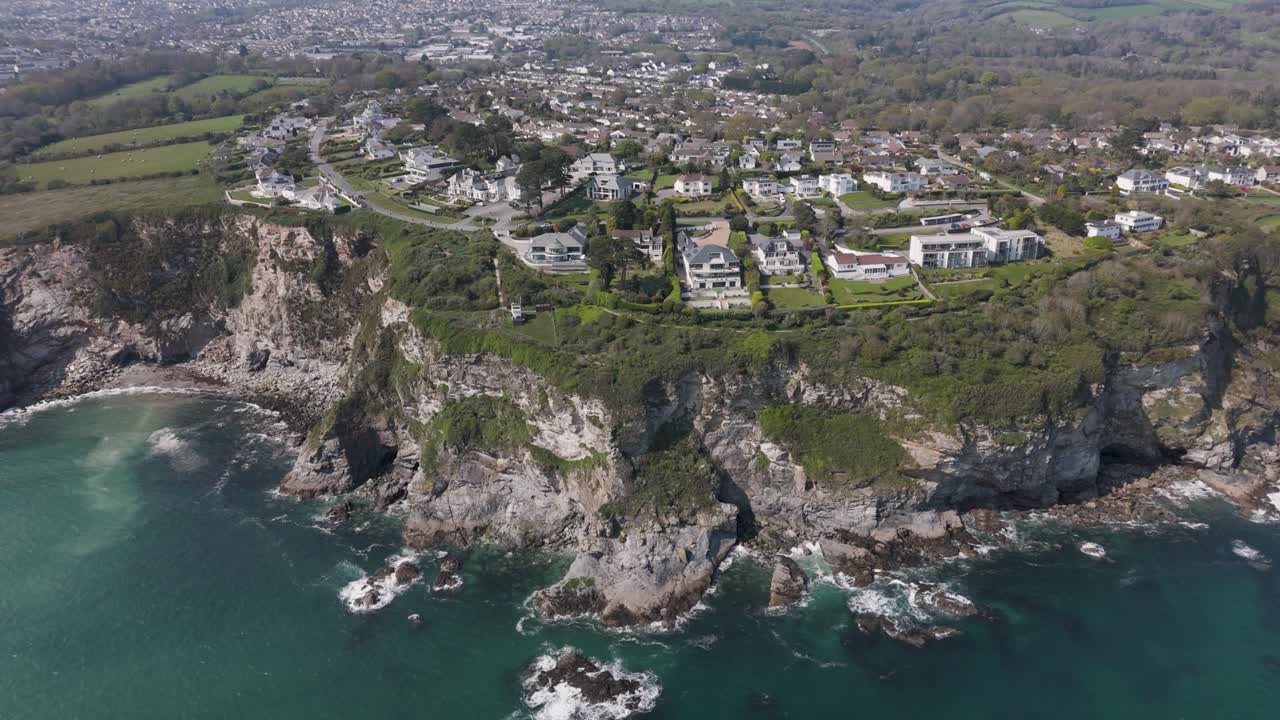 Aerial view of cliff-hugging luxury holiday villas overlooking turquoise Atlantic waves, rugged Cornish coastline and dramatic rock formations, showcasing upscale beachfront living