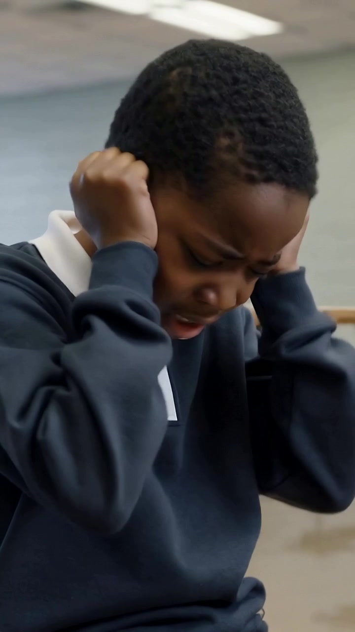 Vidéo verticale : Réagissant à un bruit soudain, un étudiant en haut marine se couvrant les oreilles à l'école, boîte transparente