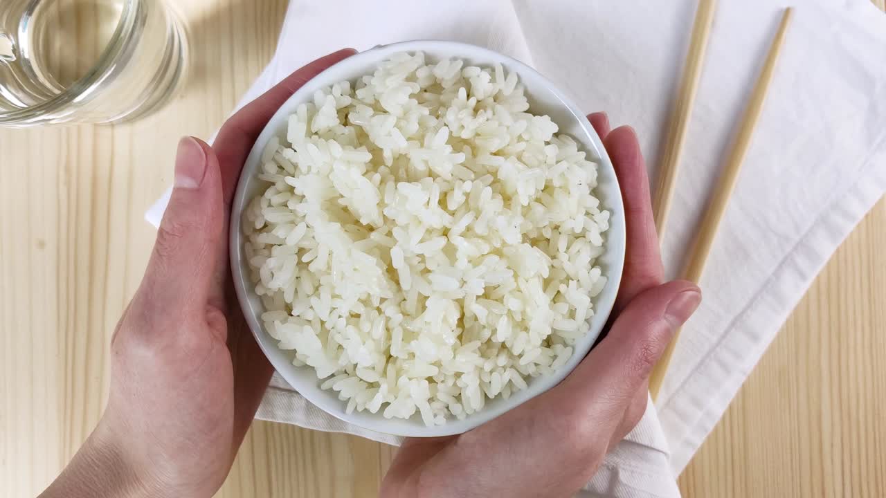 arroz blanco hervido en un cuenco redondo. las manos femeninas sostienen el plato