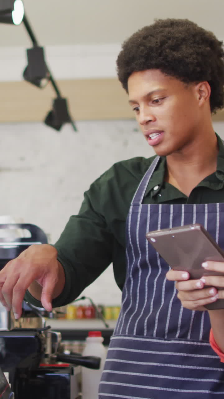 video de felices camareros femeninos y masculinos diversos en delantales trabajando con tabelet en una cafetería