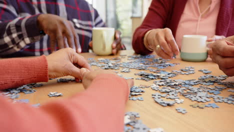 sección media de diversos amigos mayores tomando café haciendo rompecabezas en la mesa de comedor, cámara lenta